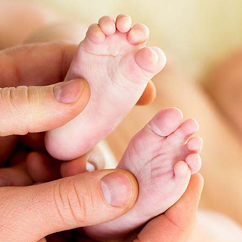The image shows a person holding a newborn baby with their feet visible, while another person s hands gently cradle the baby s feet from above.